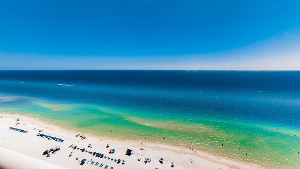 Une plage avec une eau turquoise et limpide, un rivage sablonneux, ainsi que plusieurs parasols et chaises longues.