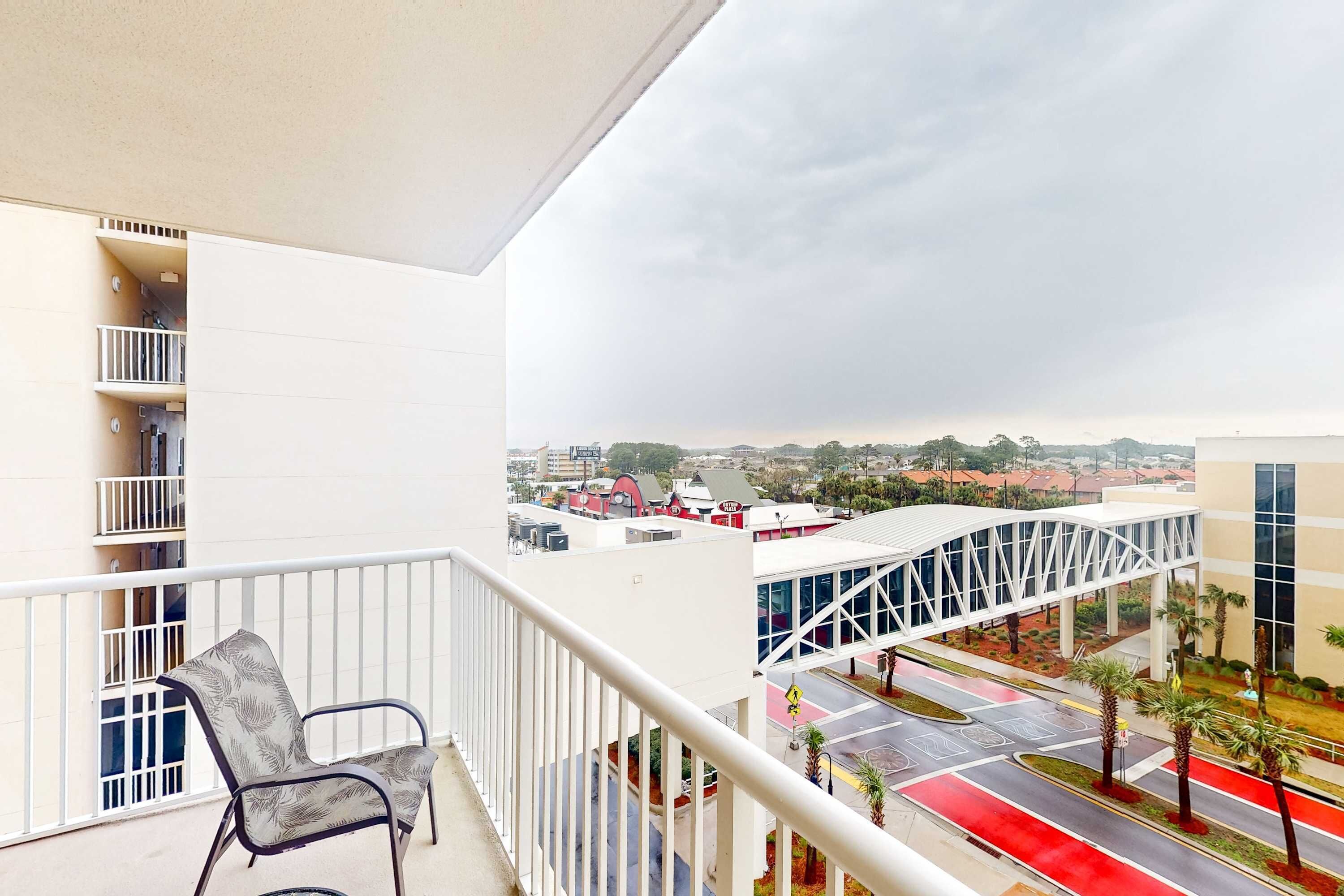 Un balcon avec une chaise, une balustrade blanche et une vue sur un paysage urbain avec des bâtiments et un pont.
