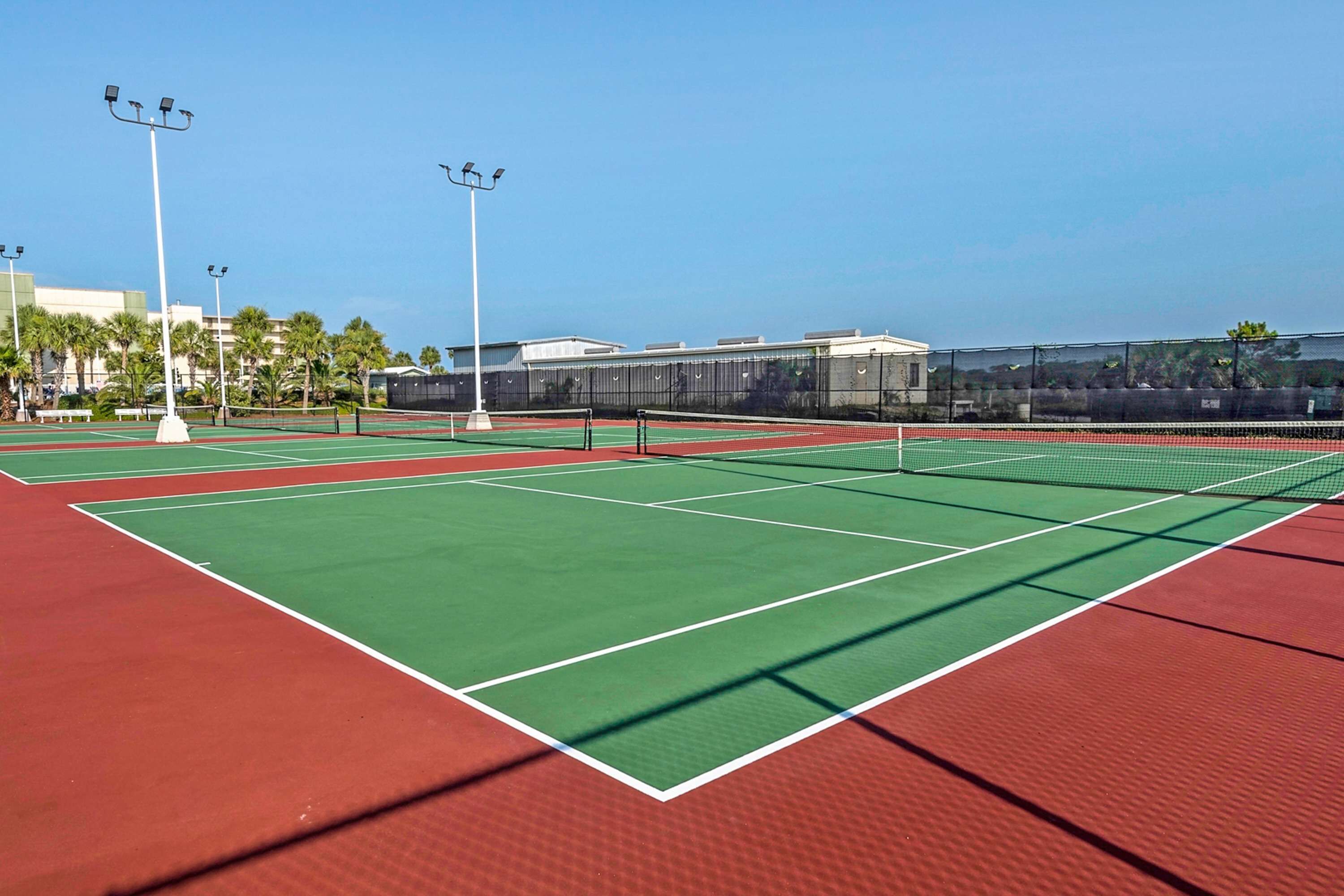 A tennis court with multiple courts, surrounded by a fence, and equipped with floodlights.