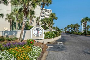 A sign for Pinnacle Port with a road leading to a building surrounded by palm trees and flower beds.