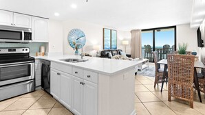 Een moderne keuken met een centraal eiland, een eetgedeelte met uitzicht, en een woonkamer met een groot raam.