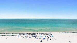 Een strand met rijen parasols en ligbedden, een heldere lucht en een kalme zee.