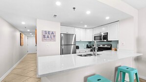 Een moderne keuken met witte kasten, roestvrijstalen apparatuur, een groot eiland met krukken, en een bordje 'SEA SALT'.