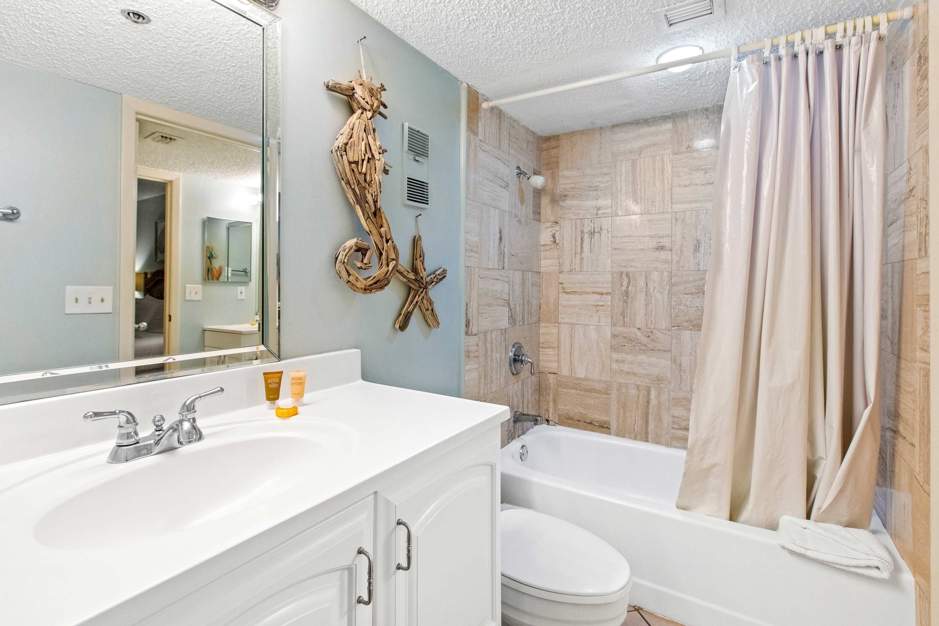 A bathroom with a white sink, two faucets, a mirror, a bathtub, and a shower curtain.