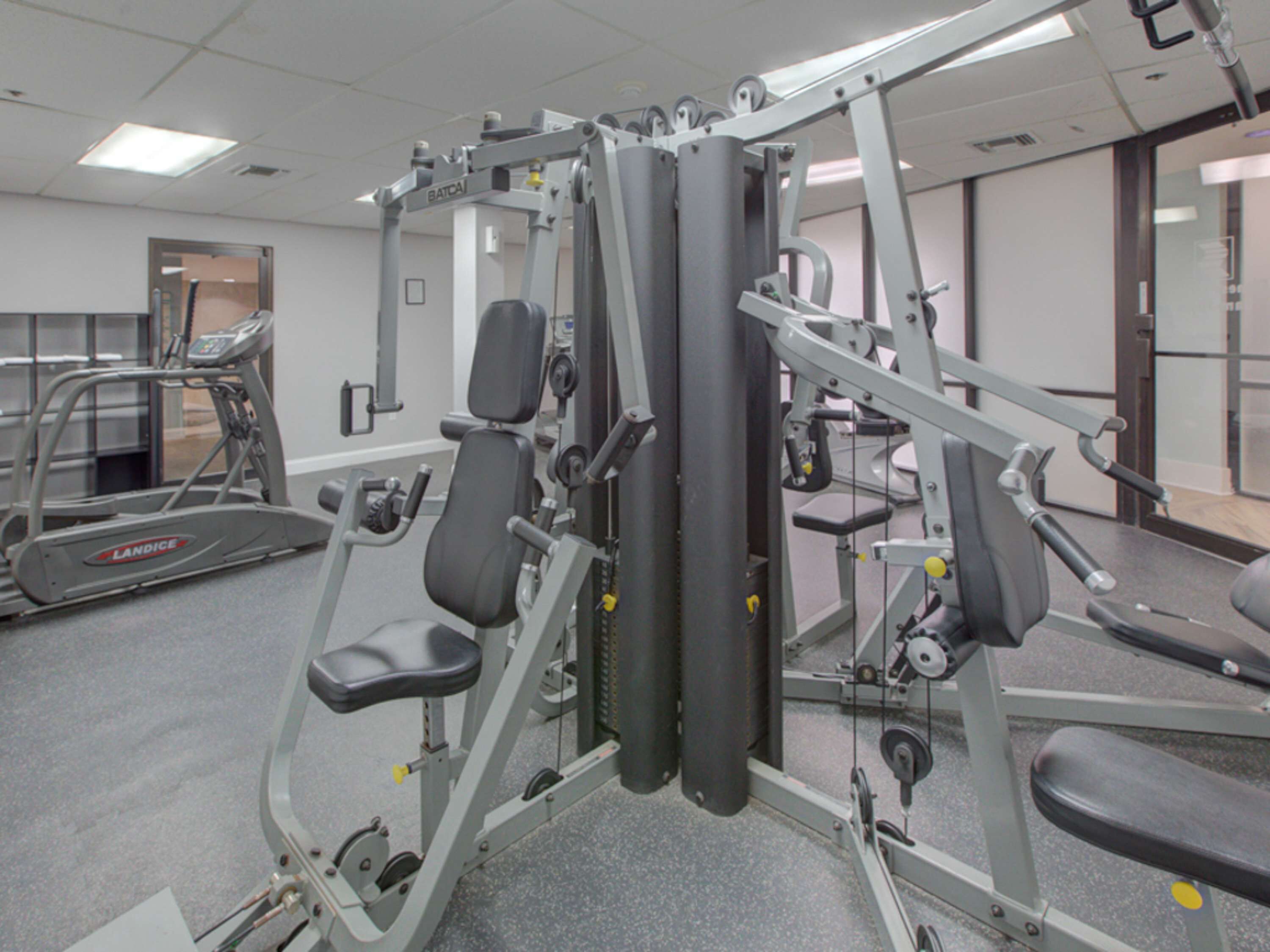 Ein Fitnessstudio mit verschiedenen Trainingsgeräten, darunter eine Hantelbank und ein Laufband.