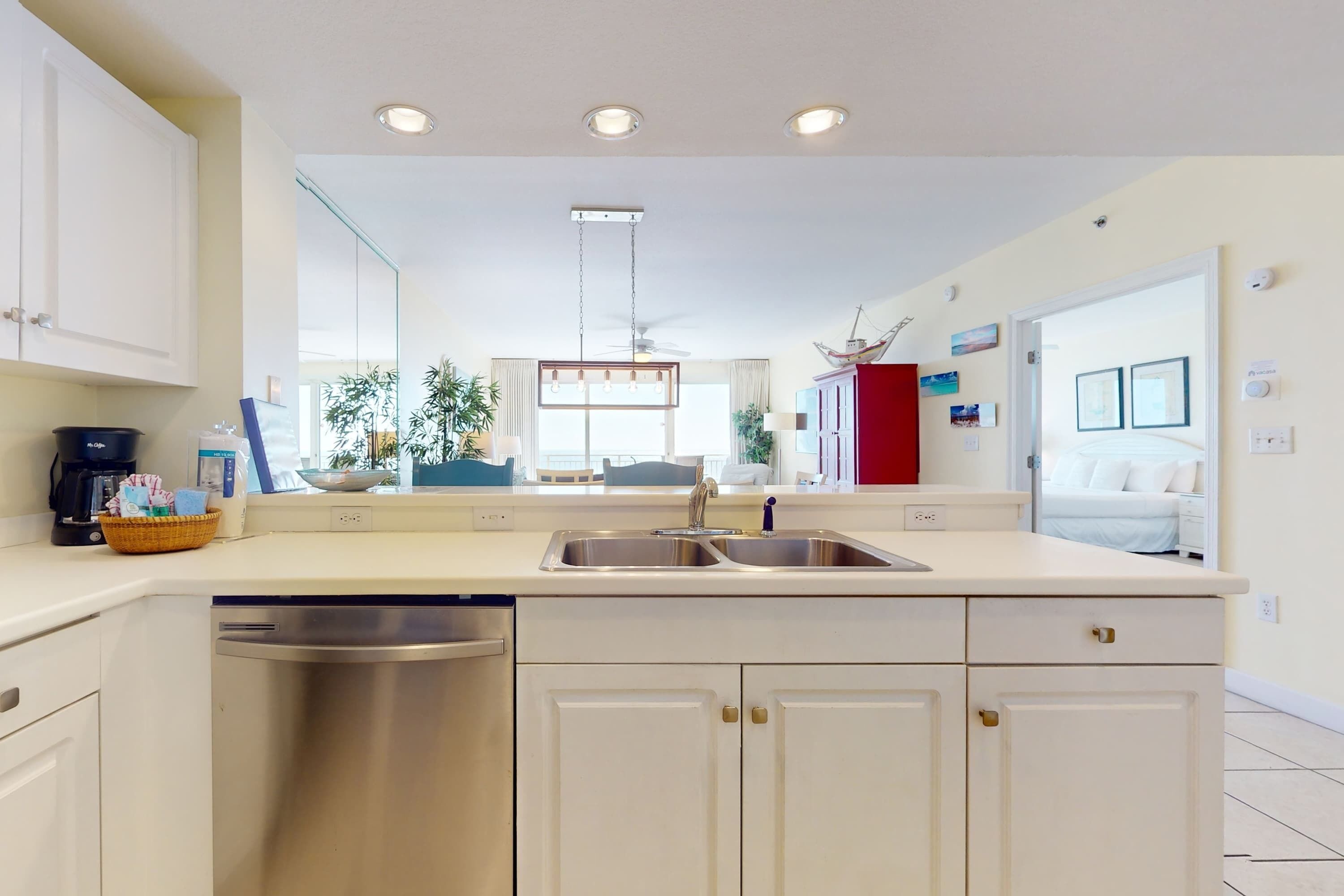 A modern kitchen with a dishwasher, double sink, and white cabinetry.