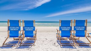 Quatro cadeiras de praia azuis com placas "Sterling Shores" em uma praia de areia.