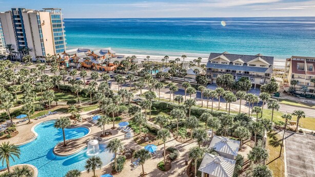 Um resort com uma piscina grande, palmeiras e vista para o oceano.