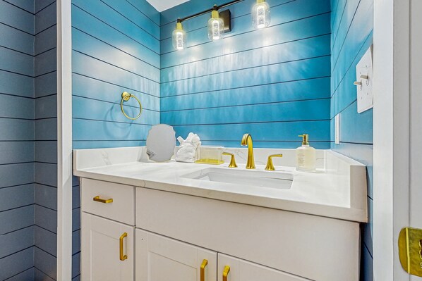 A bathroom with a white sink, gold fixtures, and a blue wall. - Oceanview condo with pool, tennis courts, beach access, laundry, & balcony (Destin)