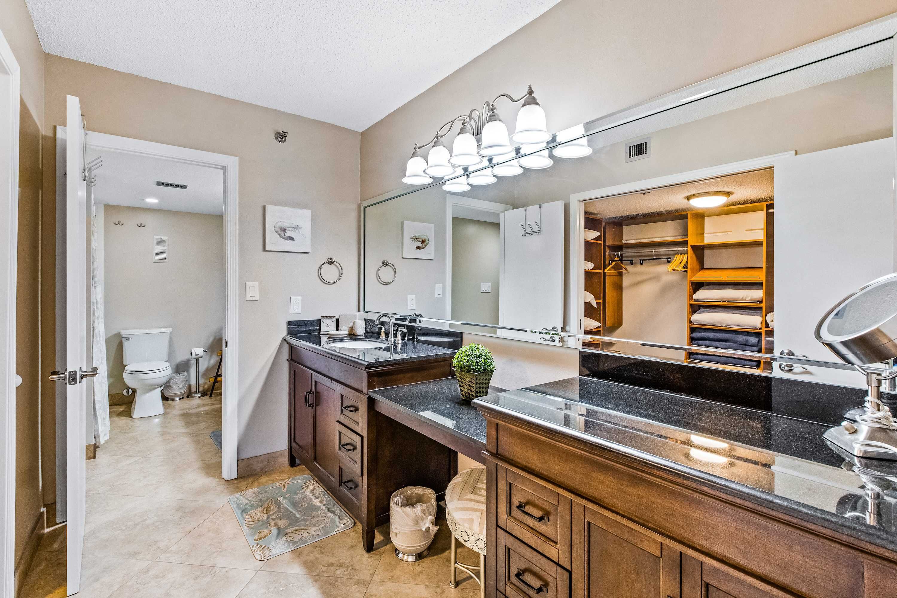 Une salle de bain moderne avec un meuble-lavabo, un évier et un miroir. On peut apercevoir des toilettes dans la pièce adjacente.