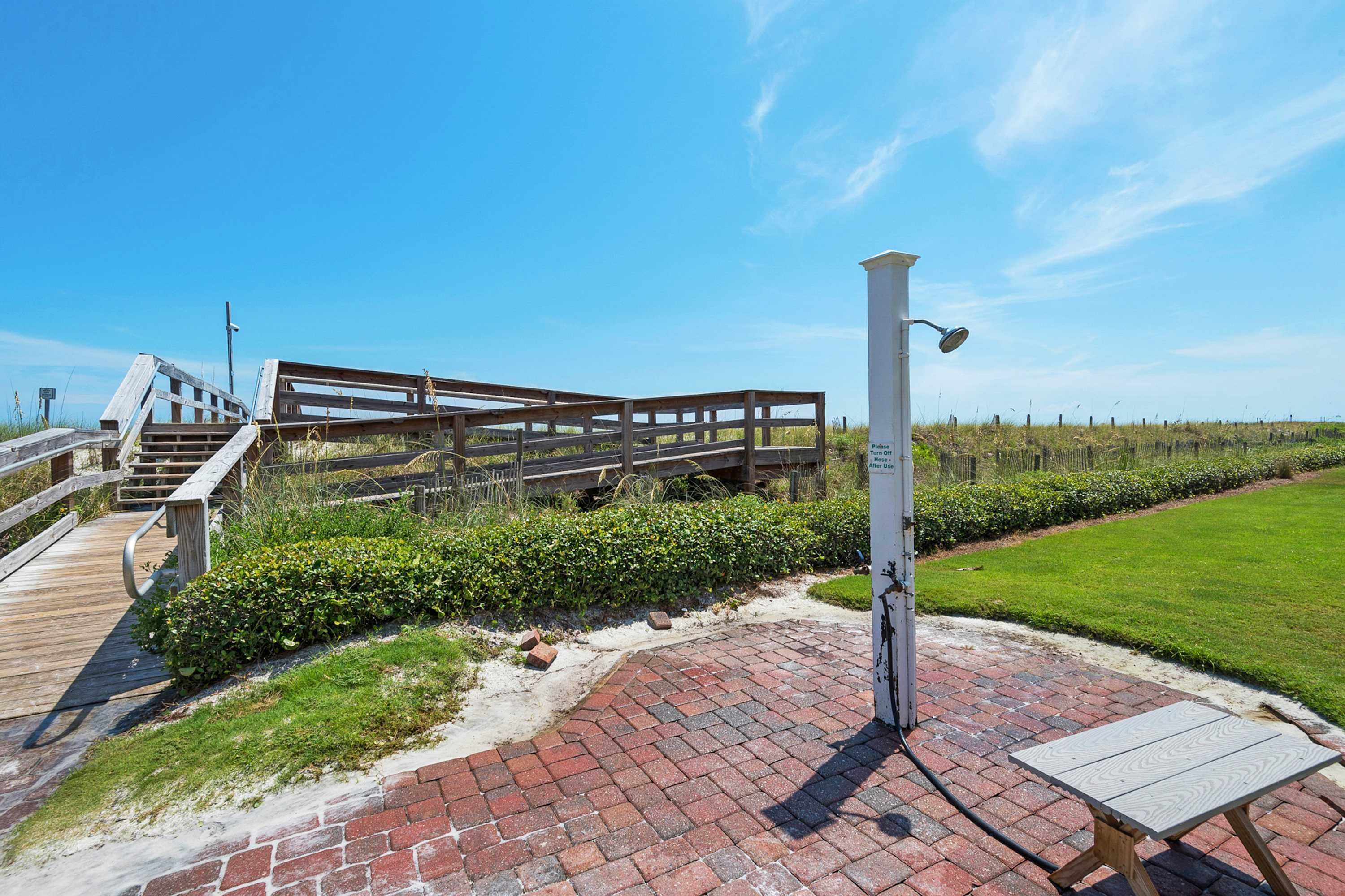A wooden deck with a metal railing, a brick pathway, and a white post with a light fixture.