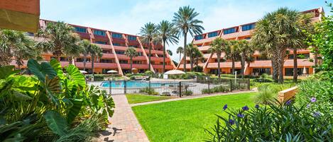 A hotel courtyard with a swimming pool, palm trees, and a brick pathway.