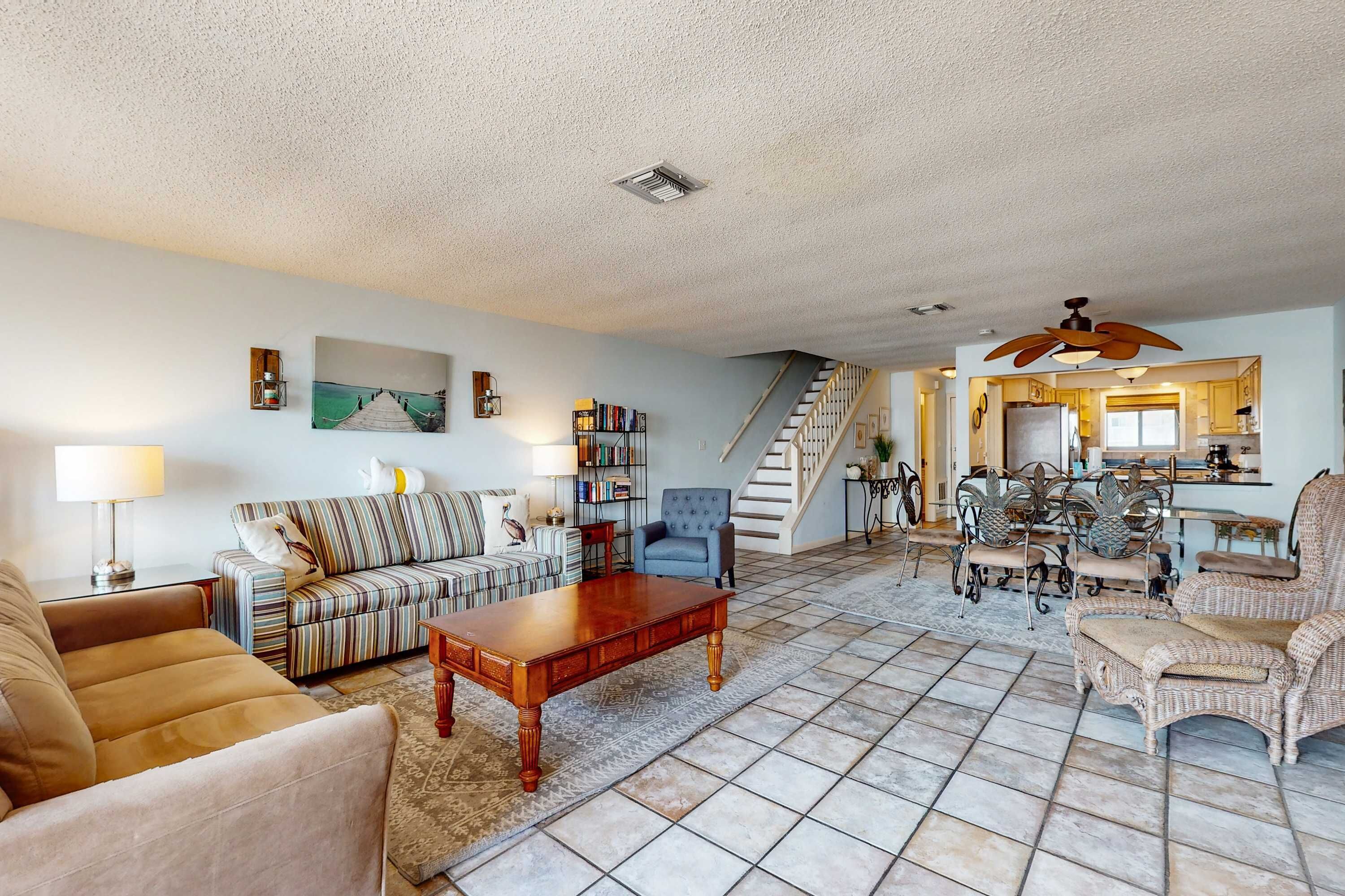 A spacious living room with a sofa, armchair, and coffee table. A staircase leads to a kitchen area.