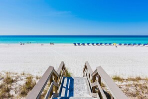Ein Strand mit einer Holztreppe zum Sand, einem klaren blauen Himmel und ruhiger See.