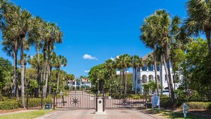 A gated entrance with a brick pathway leading to a building with a white facade and arched windows. - Destiny West - Casa Isla Paraiso (Destin)
