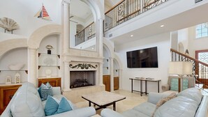 A spacious living room with a fireplace, a high ceiling, and a balcony with a railing. - Destiny West - Casa Isla Paraiso (Destin)