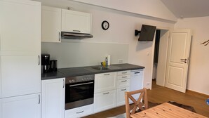 A compact kitchen with white cabinetry, a built-in oven, a coffee maker, and a wall-mounted TV.