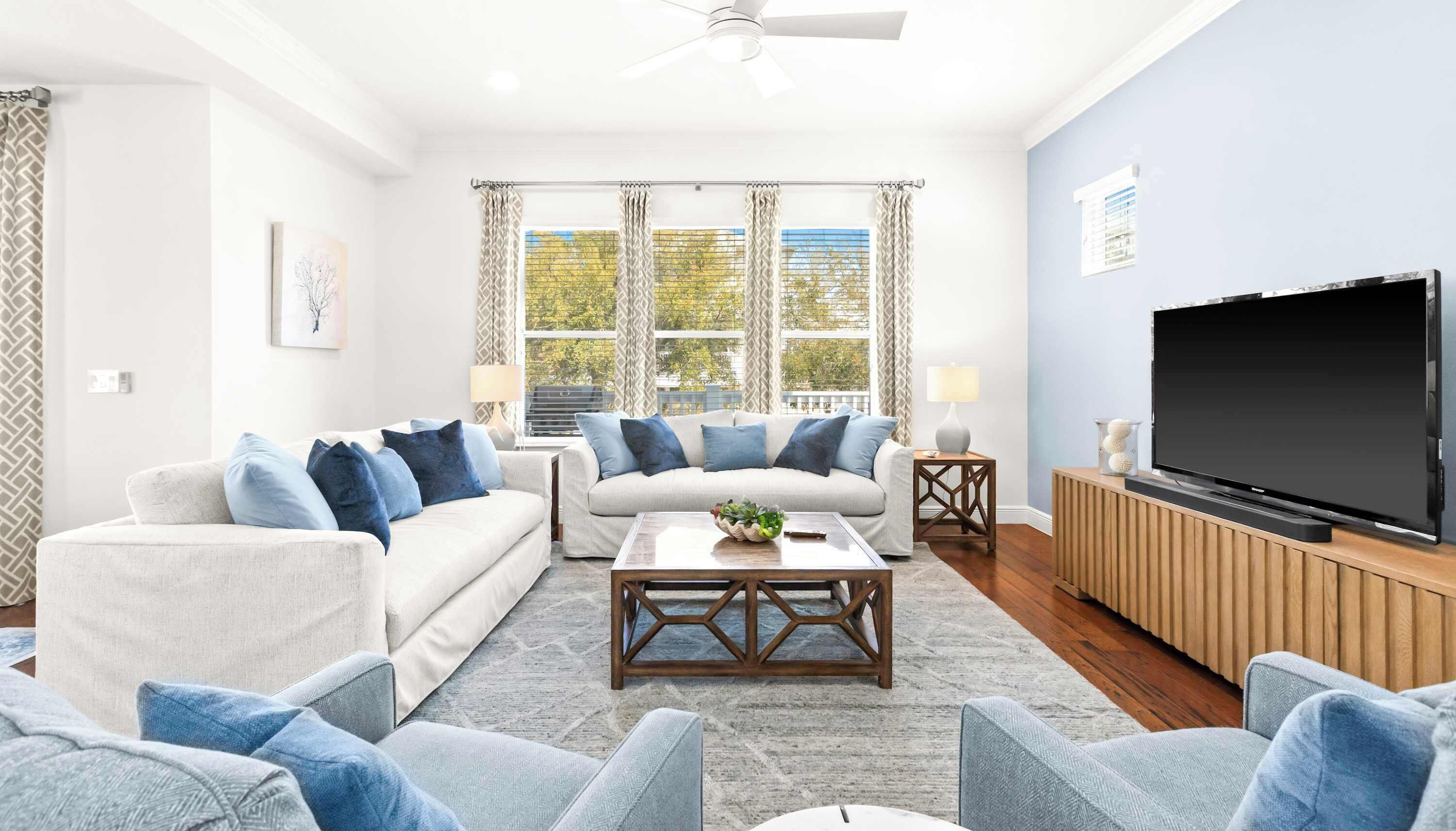 A living room with a sofa, coffee table, TV, and windows with curtains.