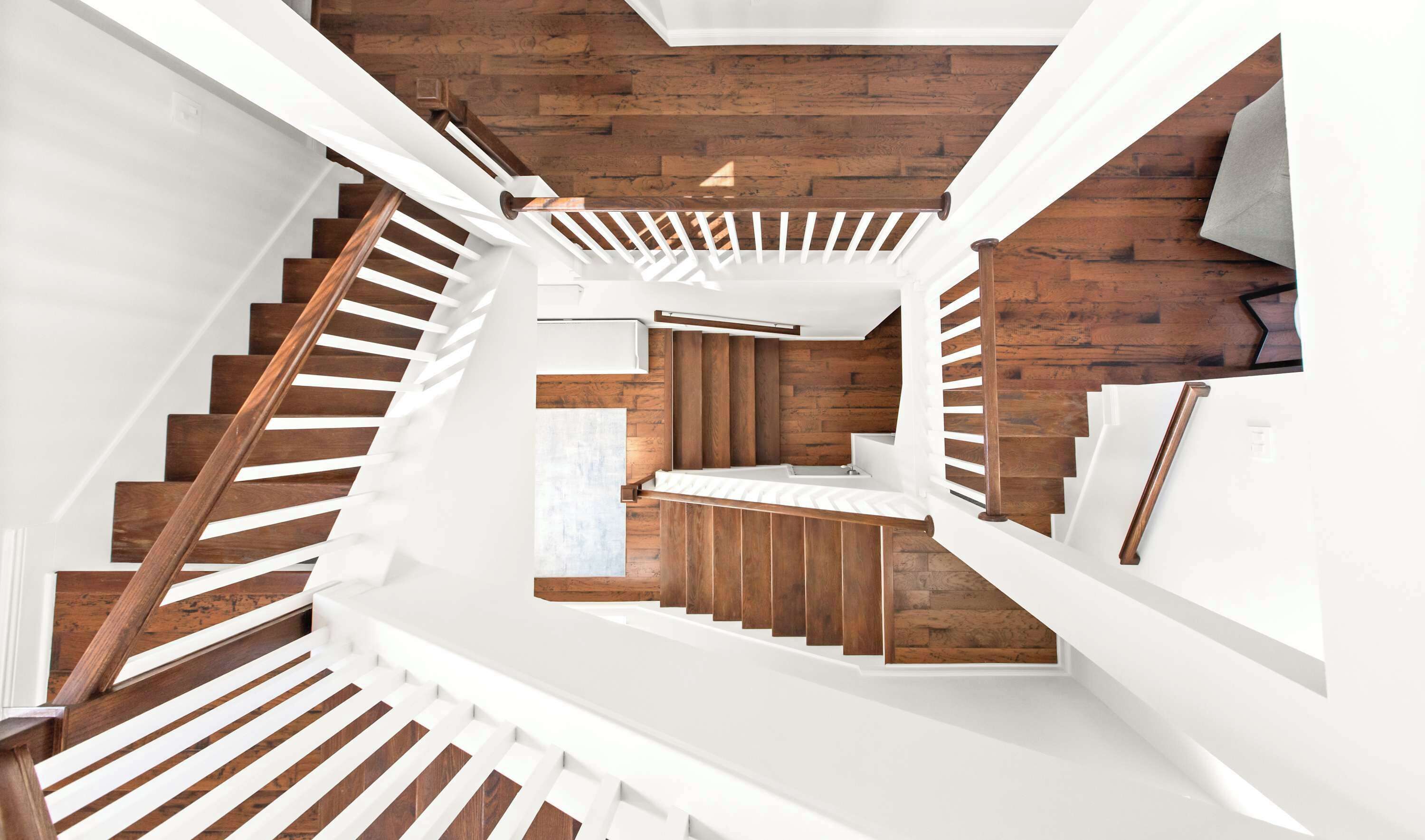 A modern staircase with wooden steps and white railings, leading to a room with a wooden wall and a white countertop.
