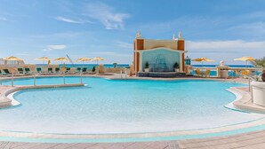 Une grande piscine extérieure dotée d’un élément décoratif central, entourée de chaises longues et de parasols.