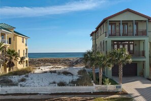 A beachfront property with a two-story building, a white picket fence, and a sandy beach. - 3-Bedroom Home Located in Destin Pointe, Near shops and dining (Destin)