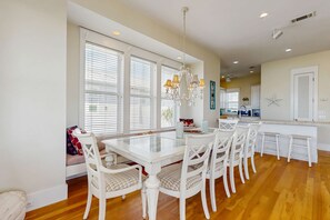 A spacious kitchen with white cabinetry, a central island, and a dining area with a glass-top table and white chairs. - 3-Bedroom Home Located in Destin Pointe, Near shops and dining (Destin)