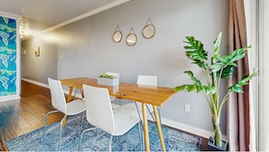 Uma sala de jantar com uma mesa de madeira, cadeiras brancas e um vaso com planta.
