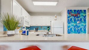 Uma cozinha moderna com armários brancos, painel de azulejos azul e decoração temática de praia.