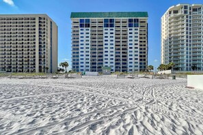 A beachfront hotel with multiple floors, a sandy beach in the foreground, and a clear blue sky. - Emerald Towers 0203 (Destin)