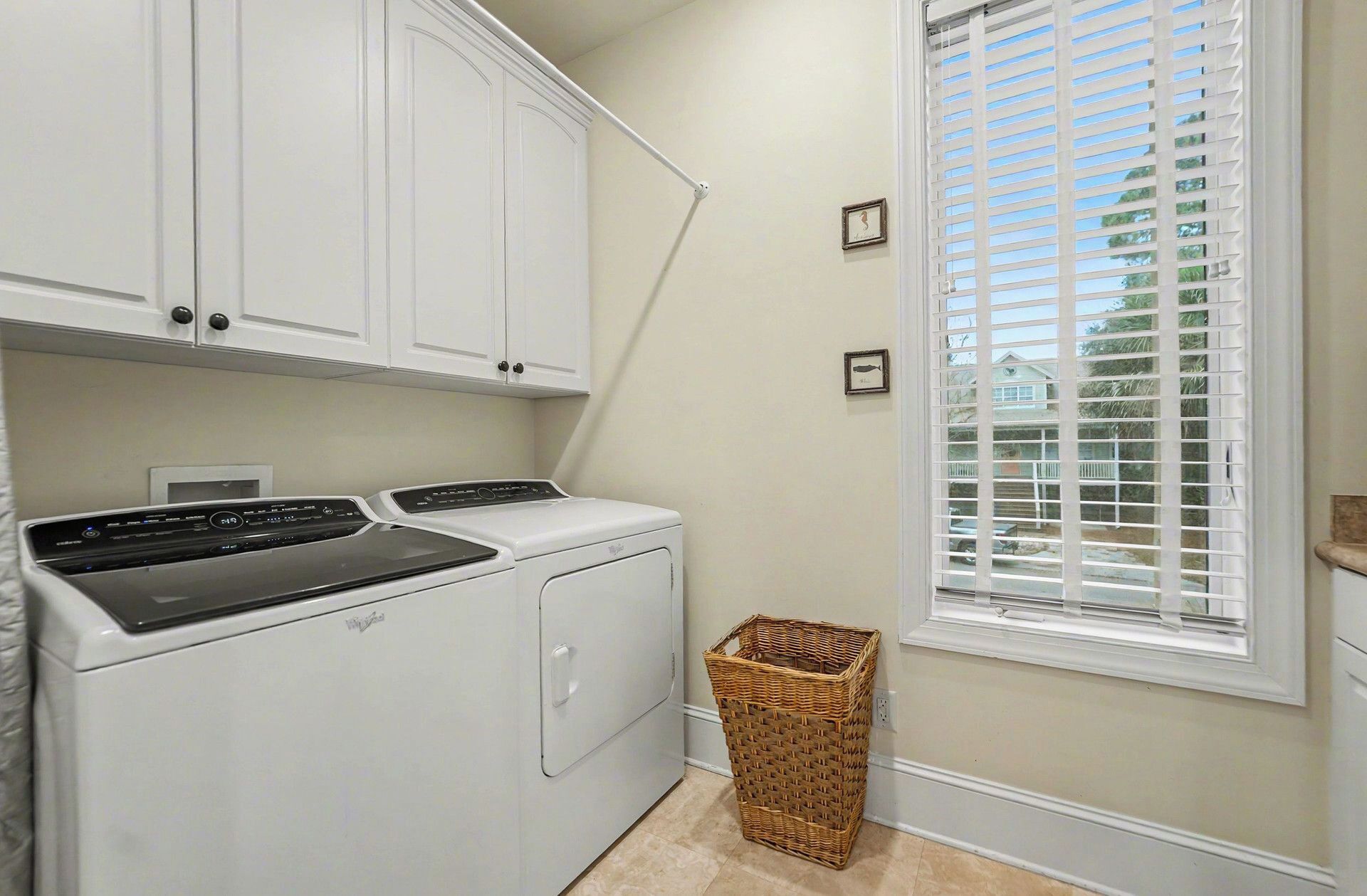 A laundry room with a front-loading washer and dryer, a wicker basket, and a window with blinds.