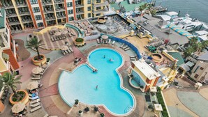 Een resort met een groot centraal zwembad, verschillende loungegedeeltes en uitzicht op de oceaan.