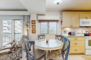 A modern kitchen with a microwave, stove, and dining area with a glass table and chairs. - Beautiful beachfront condo with shared pool and beach access (Panama City Beach)