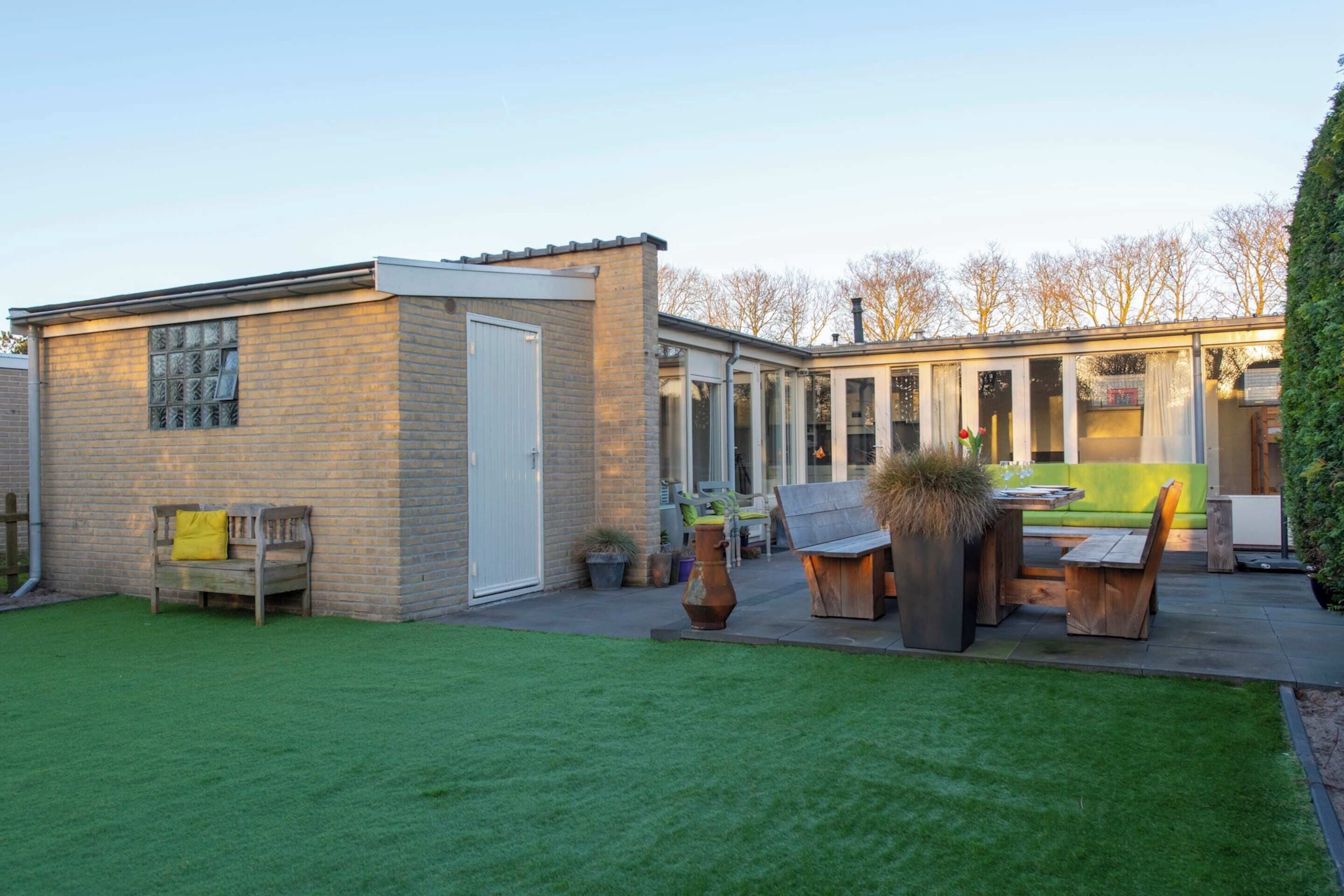 Ein modernes Haus mit Backsteinfassade, einer überdachten Terrasse und Gartenmöbeln sowie einem gepflegten Rasen.