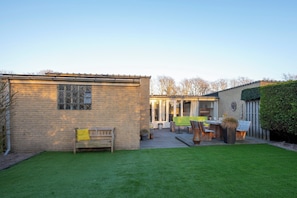 A brick house with a patio area, a wooden bench, and a dining table with chairs. - 3-bedroom House Near North Sea (Sint Maartensvlotbrug)