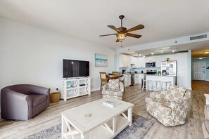 A modern living room with a sofa, armchairs, a coffee table, a TV, and a ceiling fan. - Waterfront condo with lake views, pools, putting green & shopping (Panama City Beach)