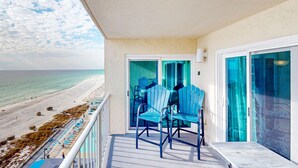 A balcony with two chairs, a view of the beach, and a glass door leading to the interior. - Beachfront Condo, gorgeous views, shared pool and beach access (Panama City Beach)