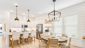 Una cocina moderna con armarios blancos, electrodomésticos de acero inoxidable y una zona de comedor con mesa y sillas redondas.