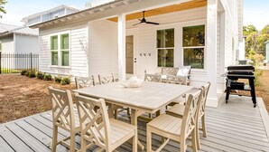 Un espacio de comedor al aire libre techado, con una mesa blanca y sillas a juego, un ventilador de techo y una parrilla.