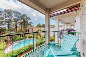 Ein Balkon mit Blick auf einen Swimmingpool, grünen Stühlen und einem Ziegeldach.