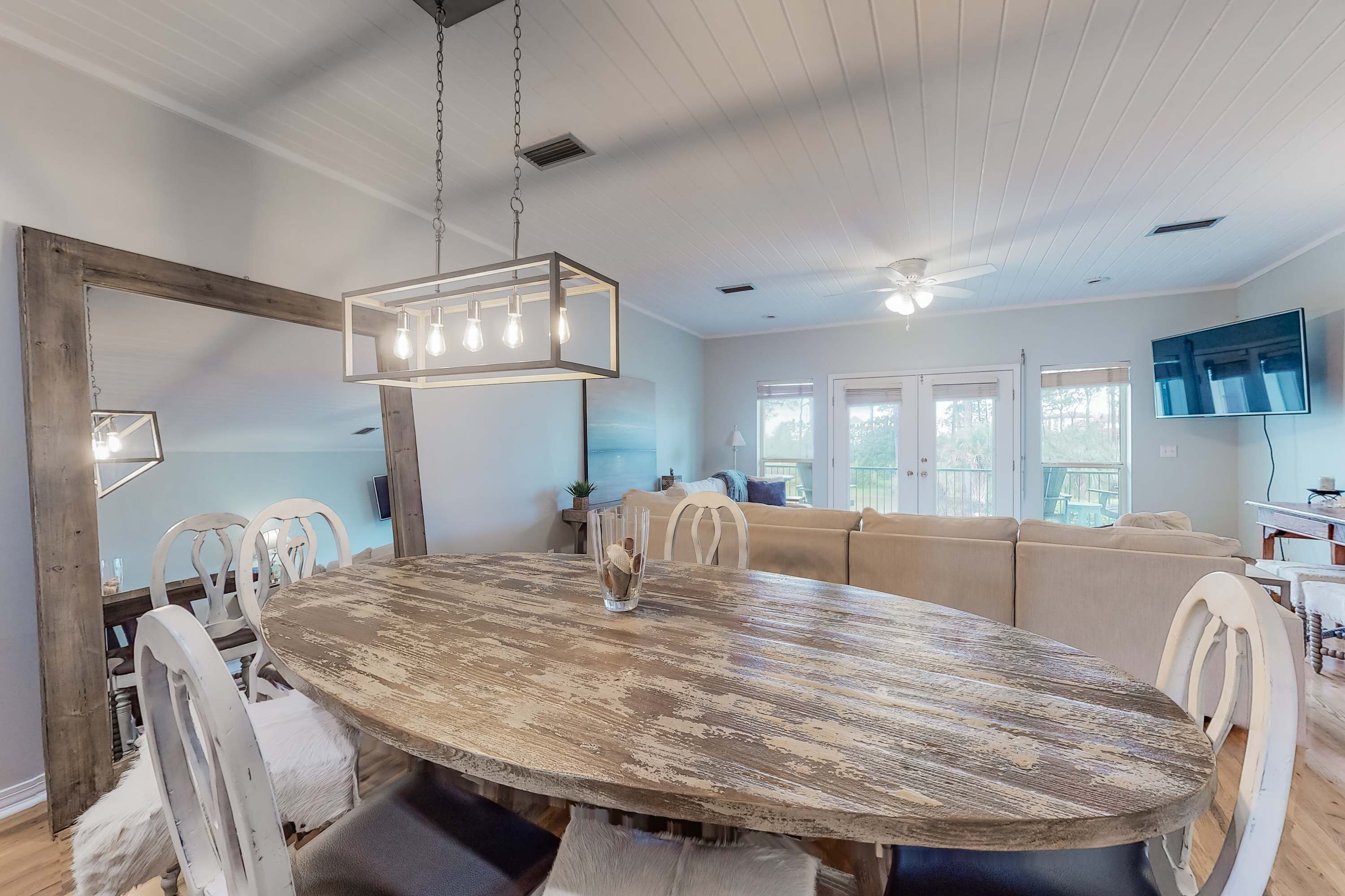 A dining area with a rustic wooden table, white chairs, and a hanging light fixture.