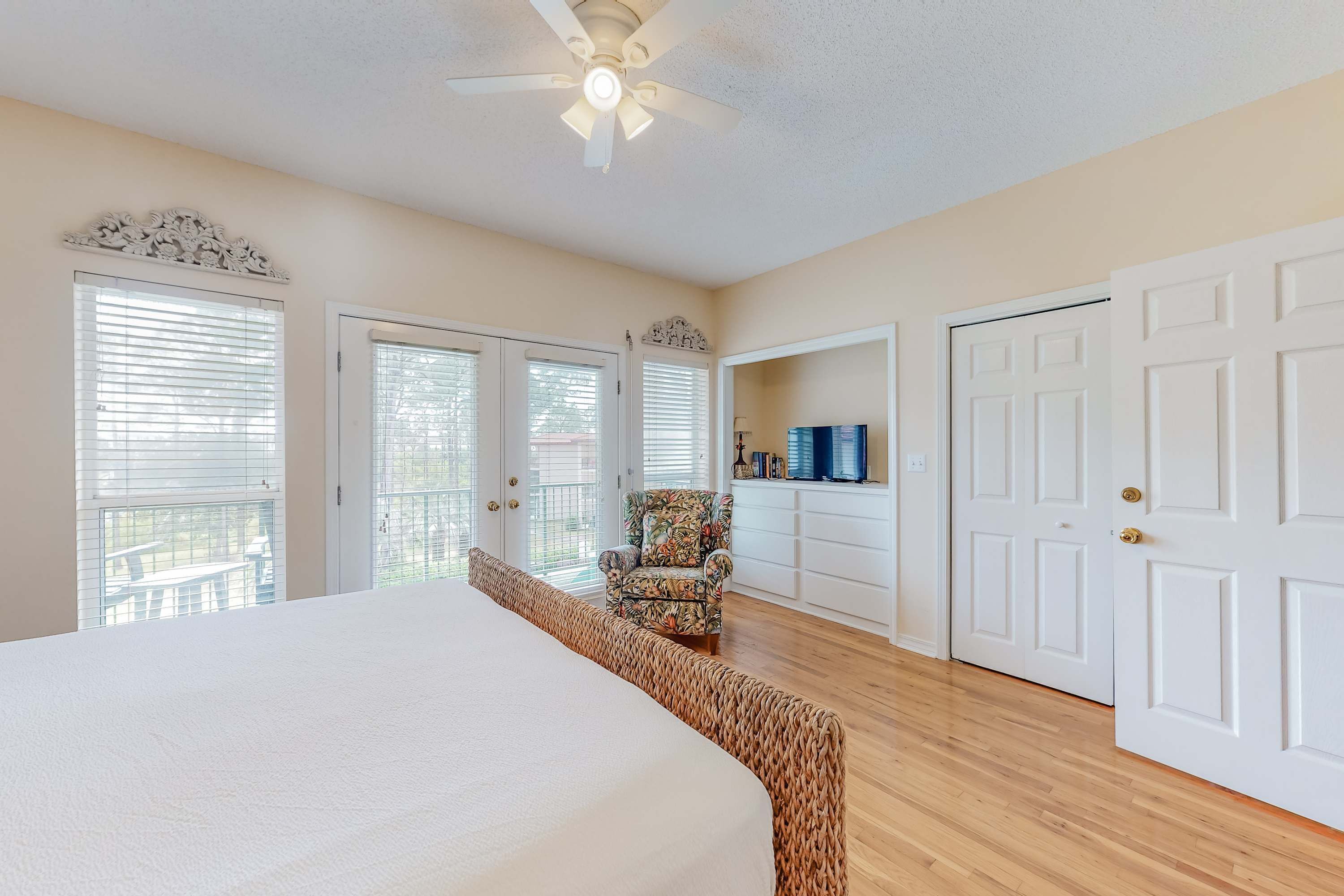 A bedroom with a large bed, a ceiling fan, and a chair. There are three doors and a window with blinds.