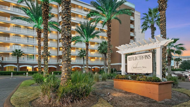 Een hotel met meerdere balkons, palmbomen en een bordje voor 'Reflections Serenity Spa'.