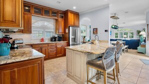 A spacious kitchen with wooden cabinets, a large island, and a dining area with bar stools. - Mangrove Mojito - Amazing Outdoor Space! (Anna Maria)
