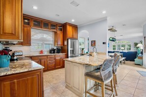 A spacious kitchen with wooden cabinets, a large island, and a dining area with bar stools. - Mangrove Mojito - Amazing Outdoor Space! (Anna Maria)