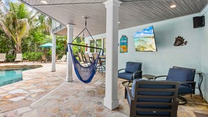A covered outdoor area with a pool, chairs, a hammock, and a bar sign. - Mangrove Mojito - Amazing Outdoor Space! (Anna Maria)