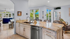 A modern kitchen with a large island, white cabinetry, and a stainless steel dishwasher. - Mangrove Mojito - Amazing Outdoor Space! (Anna Maria)