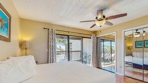 Quarto com cama grande, ventilador de teto e vista para a varanda.
