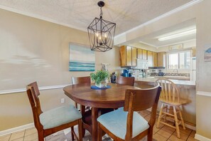 A dining area with a wooden table and chairs, a hanging light fixture, and a view into the kitchen. - 2-story resort townhouse with 3 pools, tennis, hot tub, gym, balcony, W/D, AC (Panama City Beach)