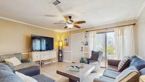 Sala de estar com televisão de tela plana, ventilador de teto e porta de vidro corrediça para o exterior.