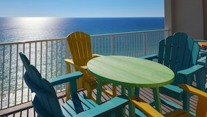 A balcony with a view of the ocean, featuring colorful Adirondack chairs and a small round table. - Stunning beachfront condo with water views, pool, hot tub, & sauna (Panama City Beach)